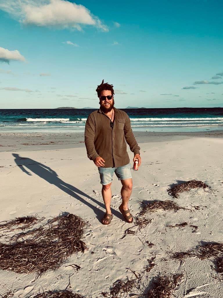 A man called Rabbit walking towards the camera wearing sunglasses on a beach.