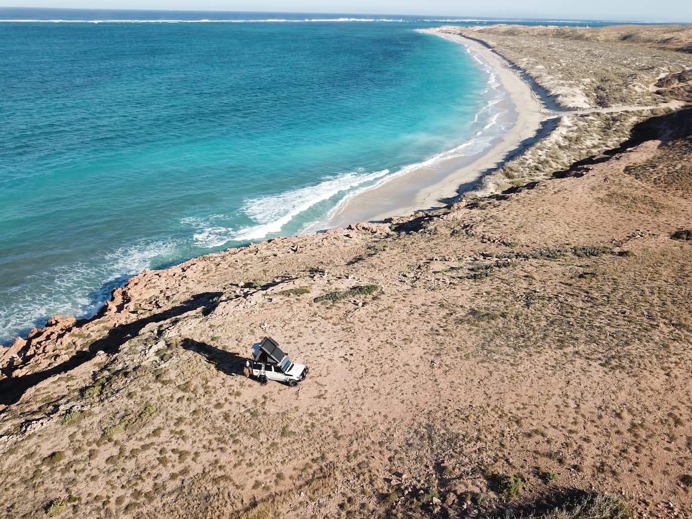 An aerial image of a 4WD on top of a coastal cliff limestone face with the ocean and beach in the background.