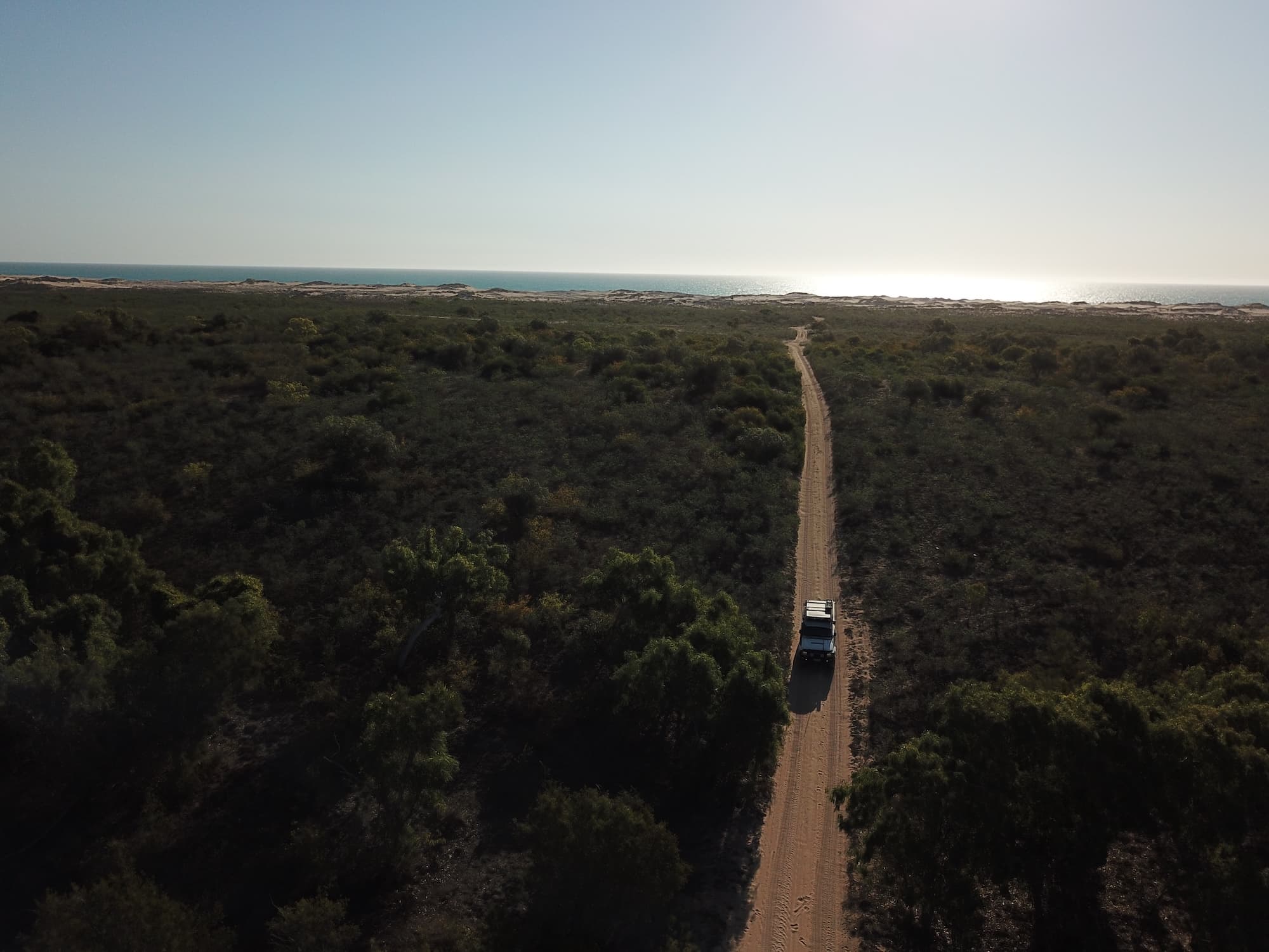 Aerial photo of a 4WD driving away from the coast on a dirt road surrounded by Australian coastal scrubland